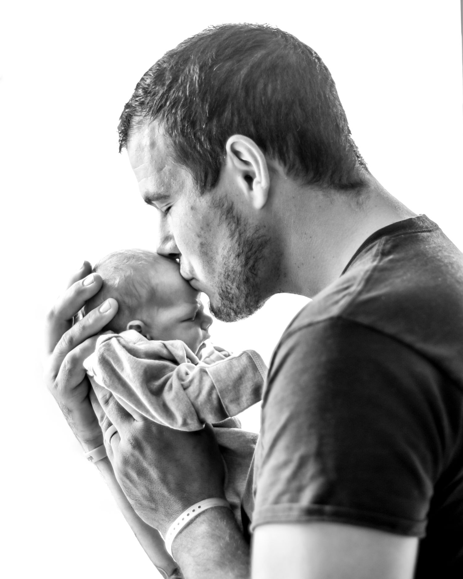 Black and white portrait of a tender moment between a parent and newborn baby in a gentle embrace.