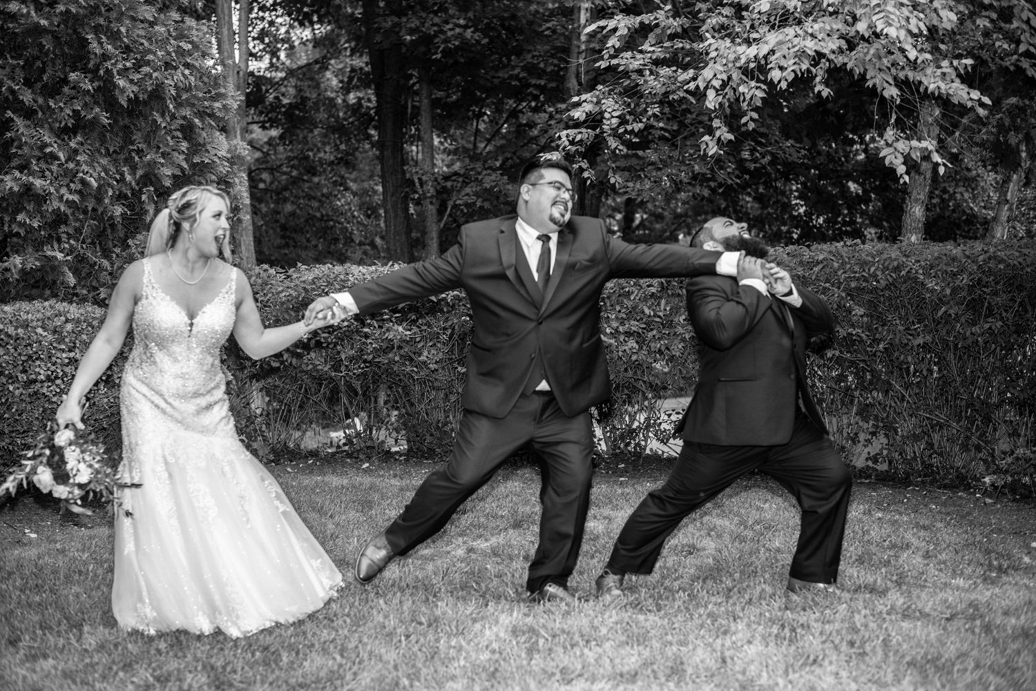 A playful wedding party strikes dramatic poses on a grassy lawn in black and white.