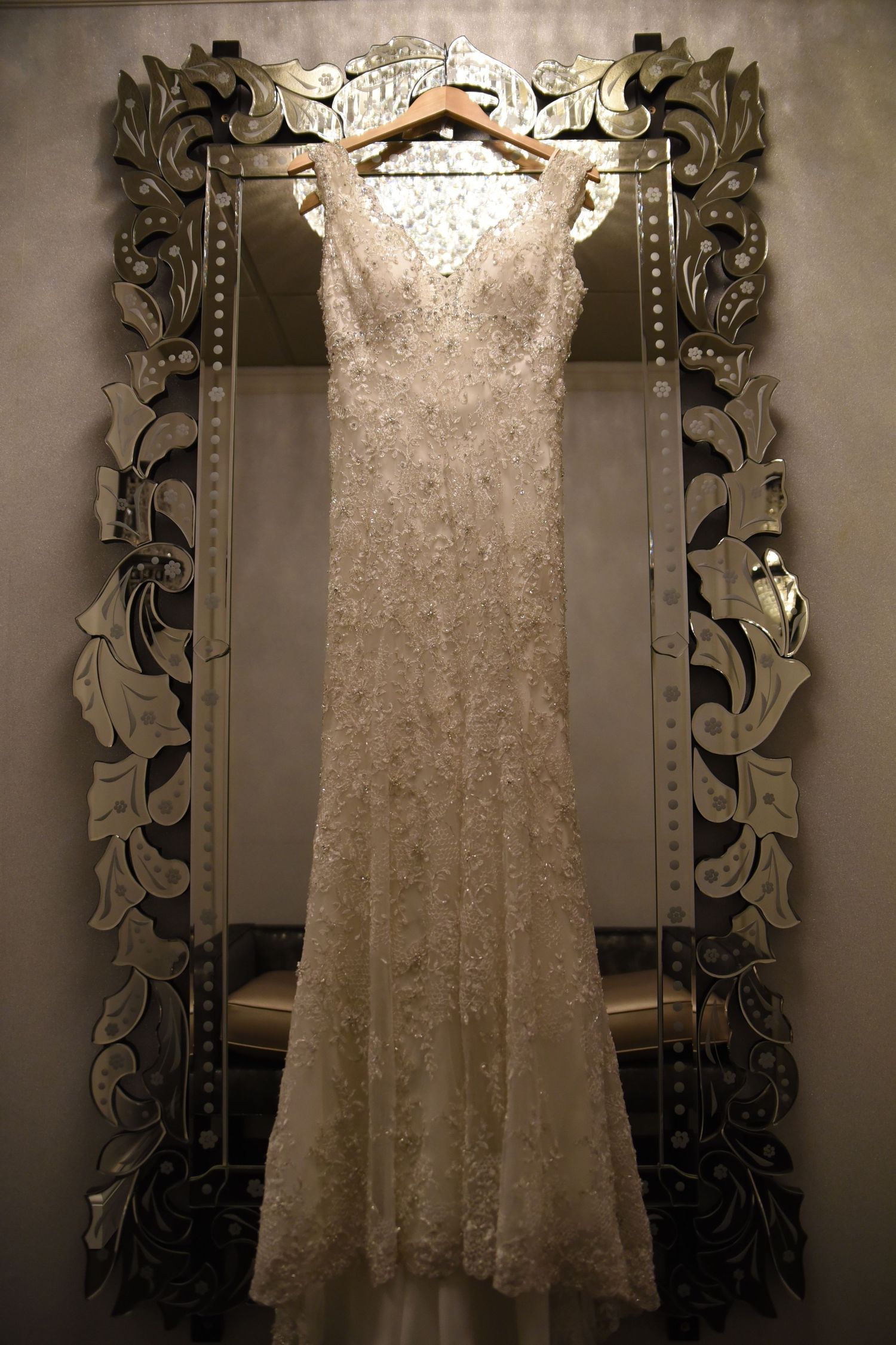 A lace wedding gown displayed against an ornate vintage mirror.