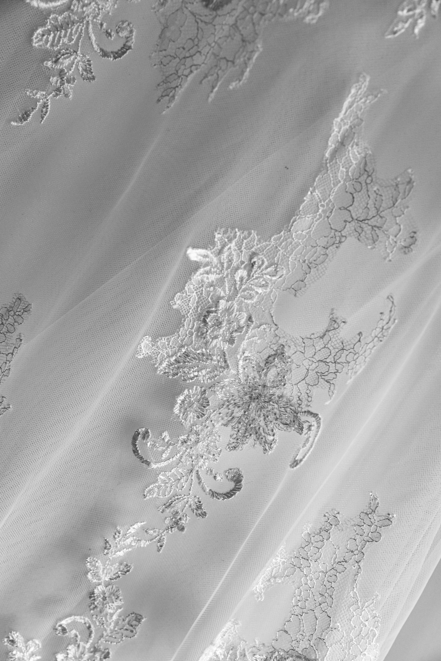 Close-up detail of delicate white lace embroidery on wedding dress fabric.