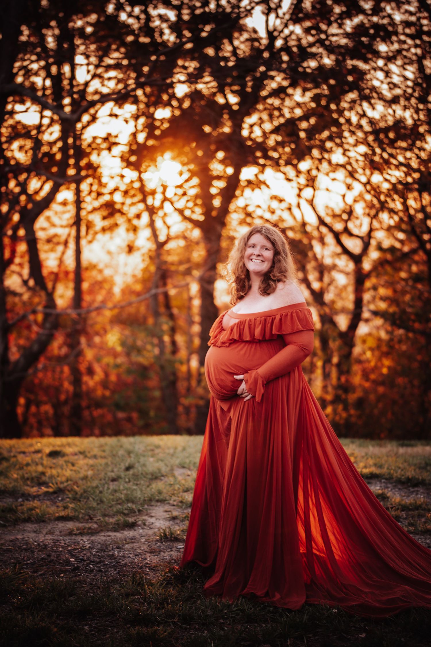 Silhouetted figures in flowing red dresses stand against a warm autumn sunset through trees creating a magical scene.