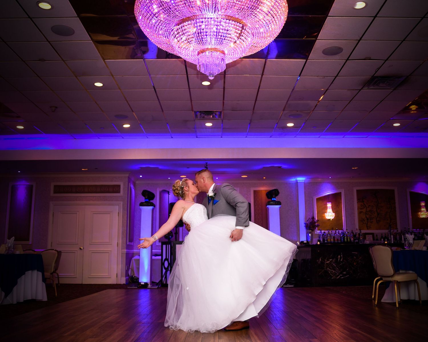 Wedding reception ballroom with purple uplighting and crystal chandelier.