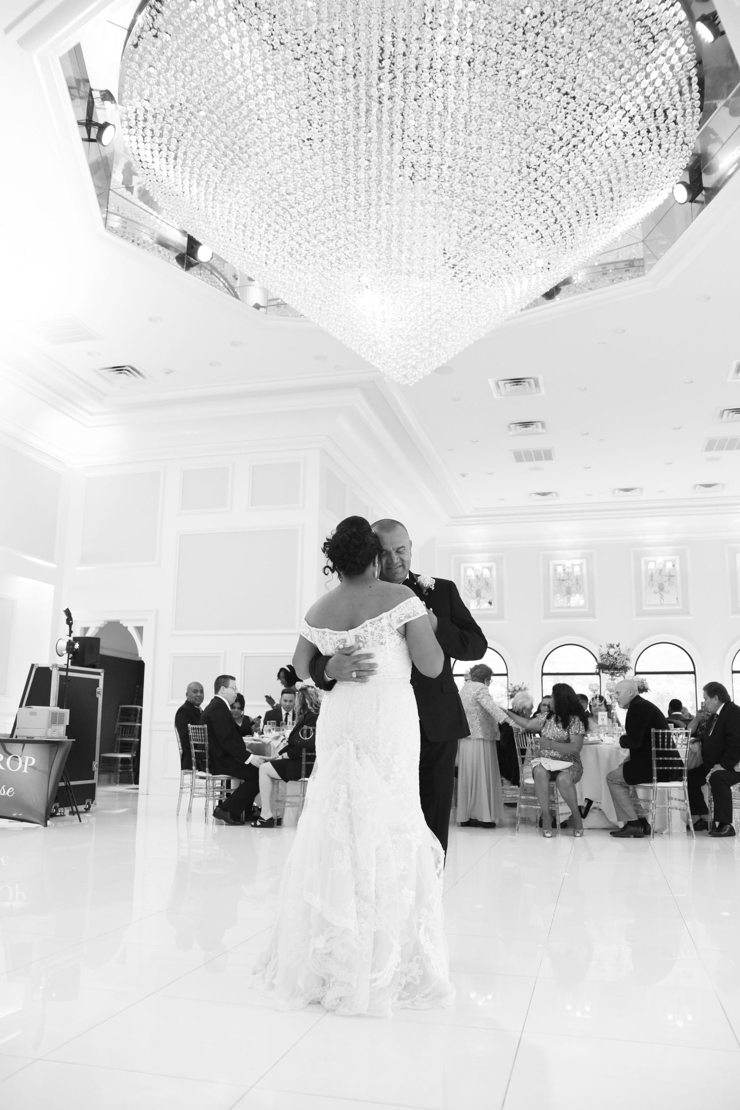 Black and white photo of couple's first dance under crystal chandelier in elegant ballroom.