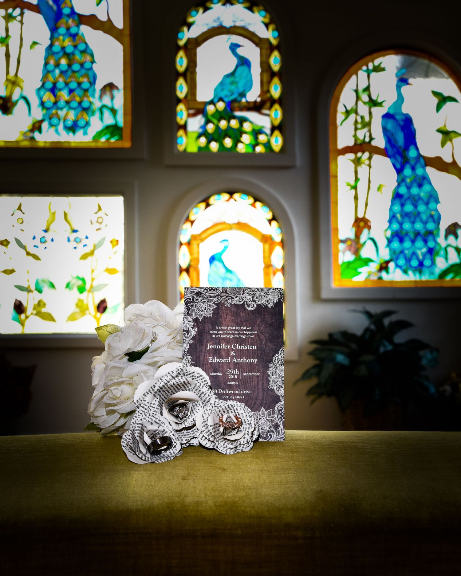 Wedding invitations displayed against colorful stained glass windows with peacock designs.