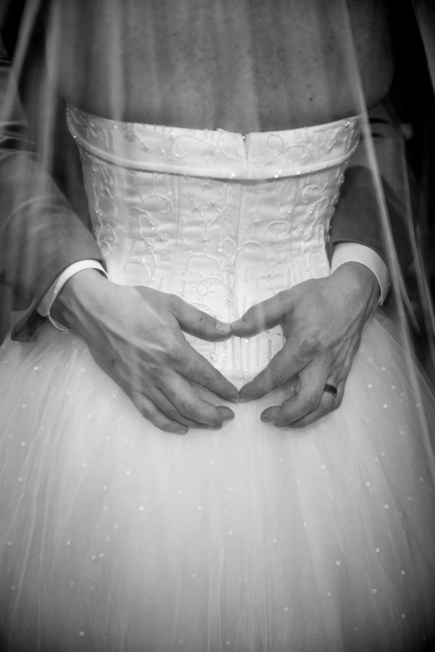 Close-up detail shot of white wedding dress bodice and hands.