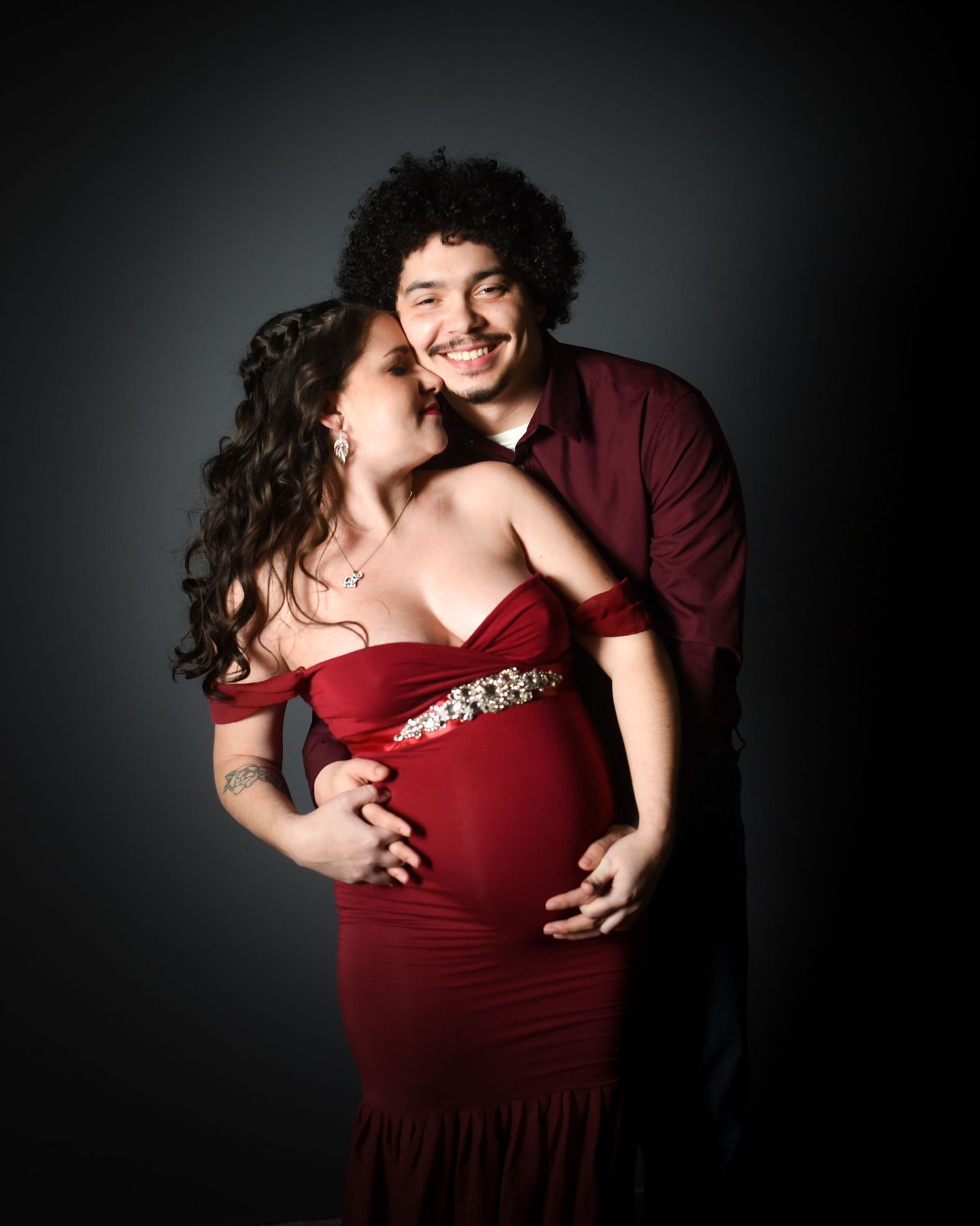 A couple embraces intimately in a series of romantic portraits against a dark background wearing burgundy attire.