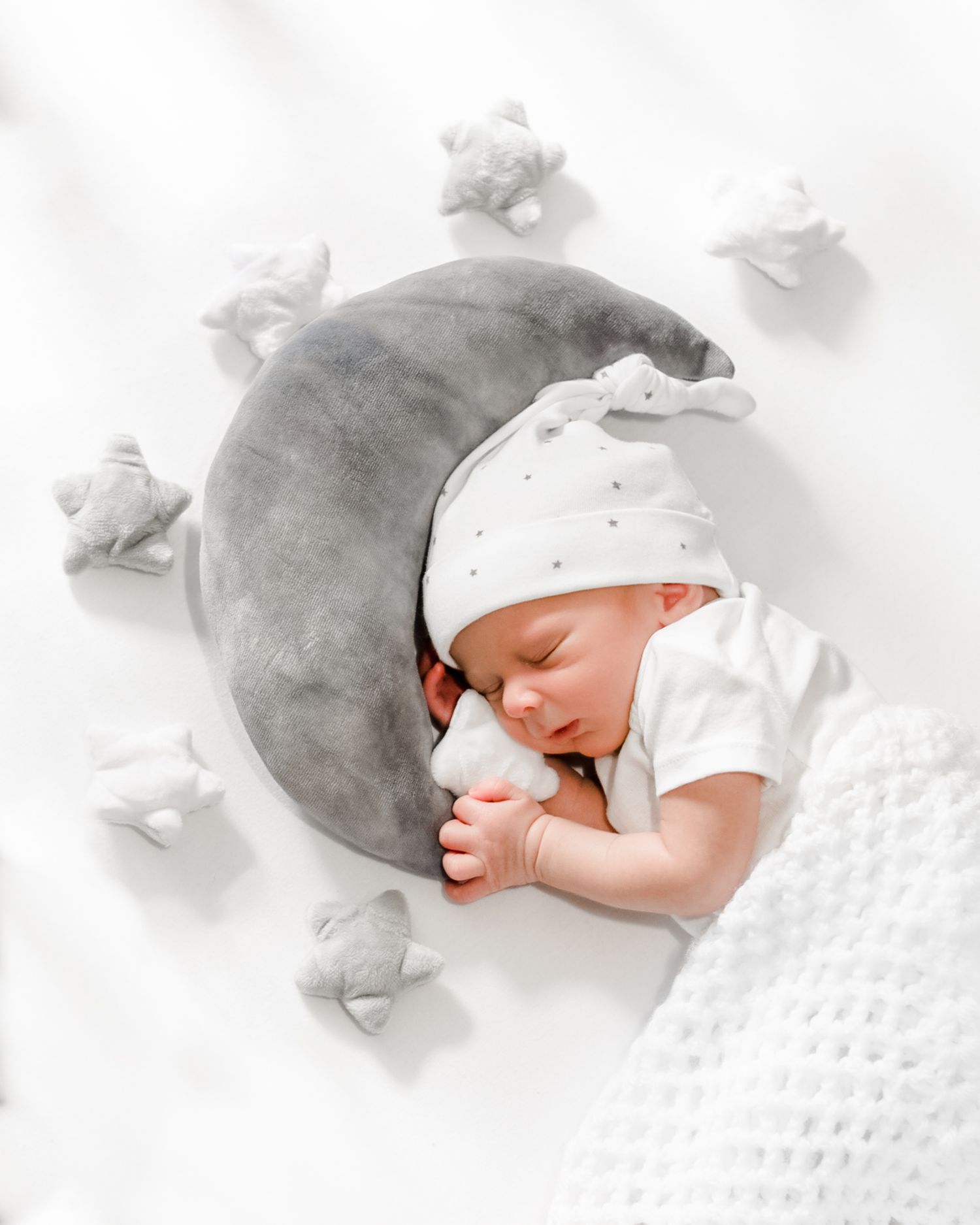 Sleeping newborn baby in white blanket and hat photographed in soft black and white tones.