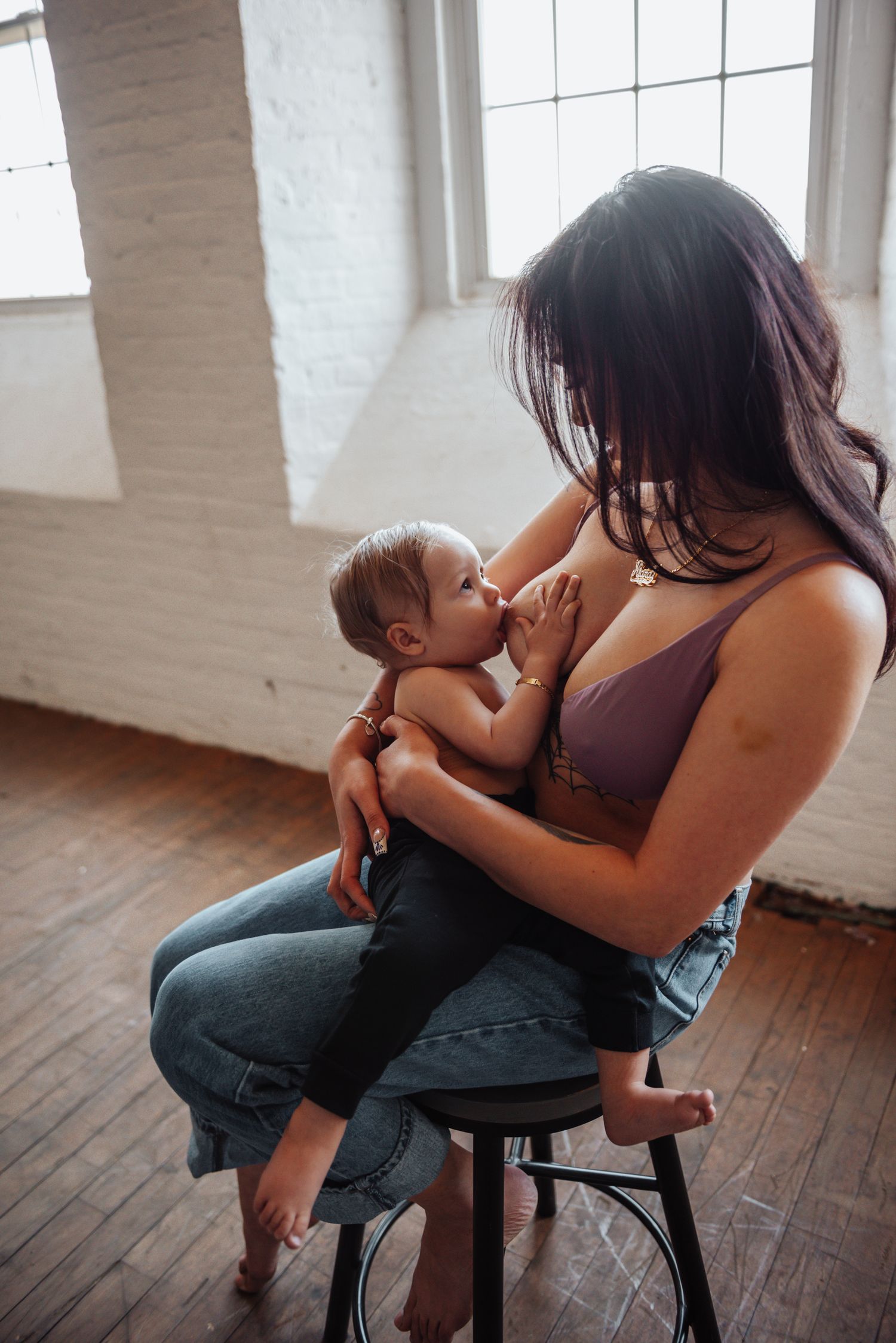 A tender moment between mother and child sitting on a wooden stool in a bright sunlit room.