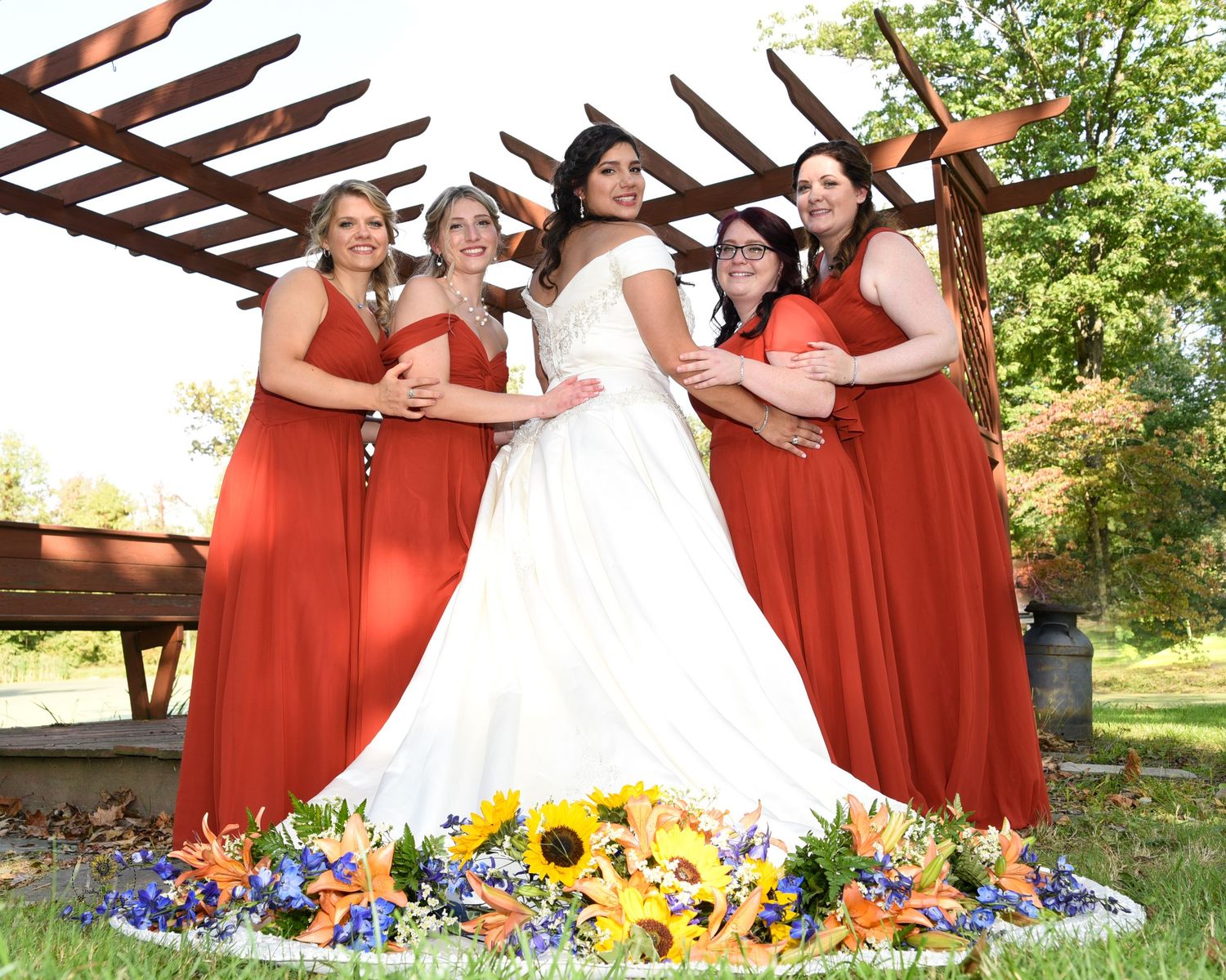 Wedding party poses outdoors with bride in white and bridesmaids in red dresses with sunflowers.