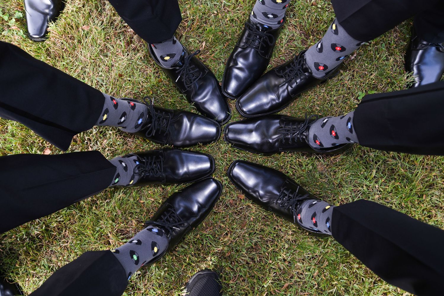 Creative overhead shot of dress shoes arranged in circular pattern on grass.