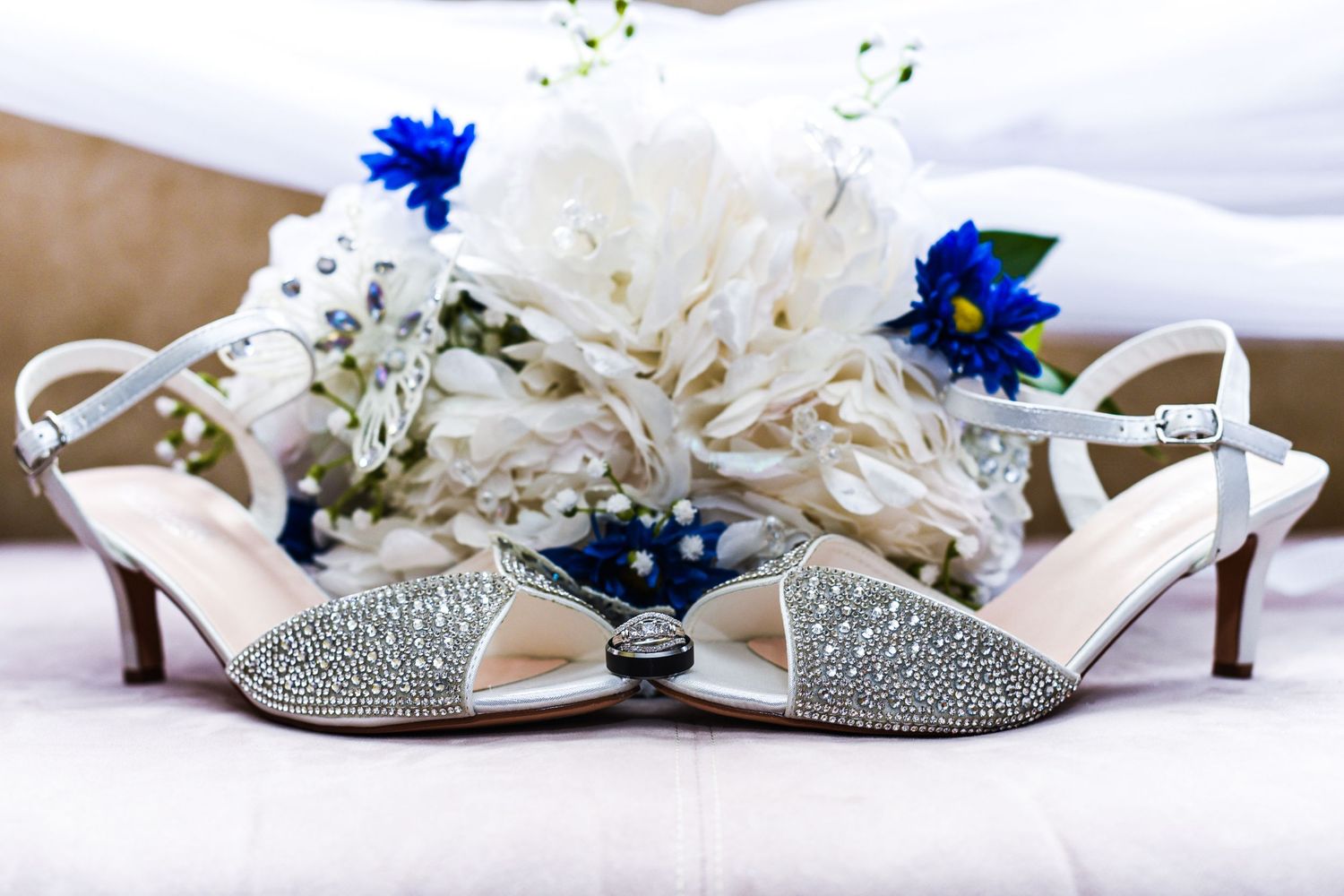Sparkly bridal shoes and delicate floral accessories arranged on white fabric.