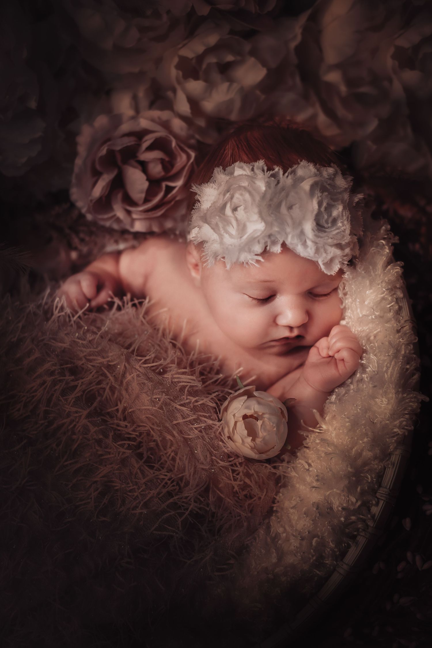 Sleeping newborn baby nestled in soft pink and cream textured blankets with dramatic lighting and dark background.