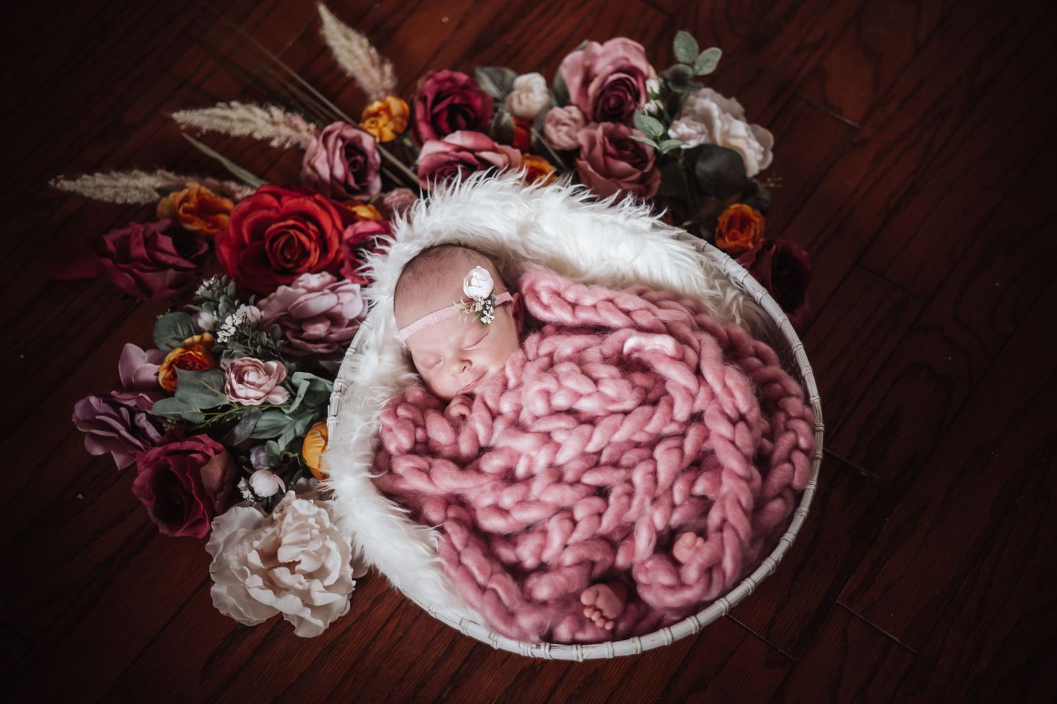 Pink whipped cream swirls in a white ceramic bowl surrounded by dark red roses and floral decorations.