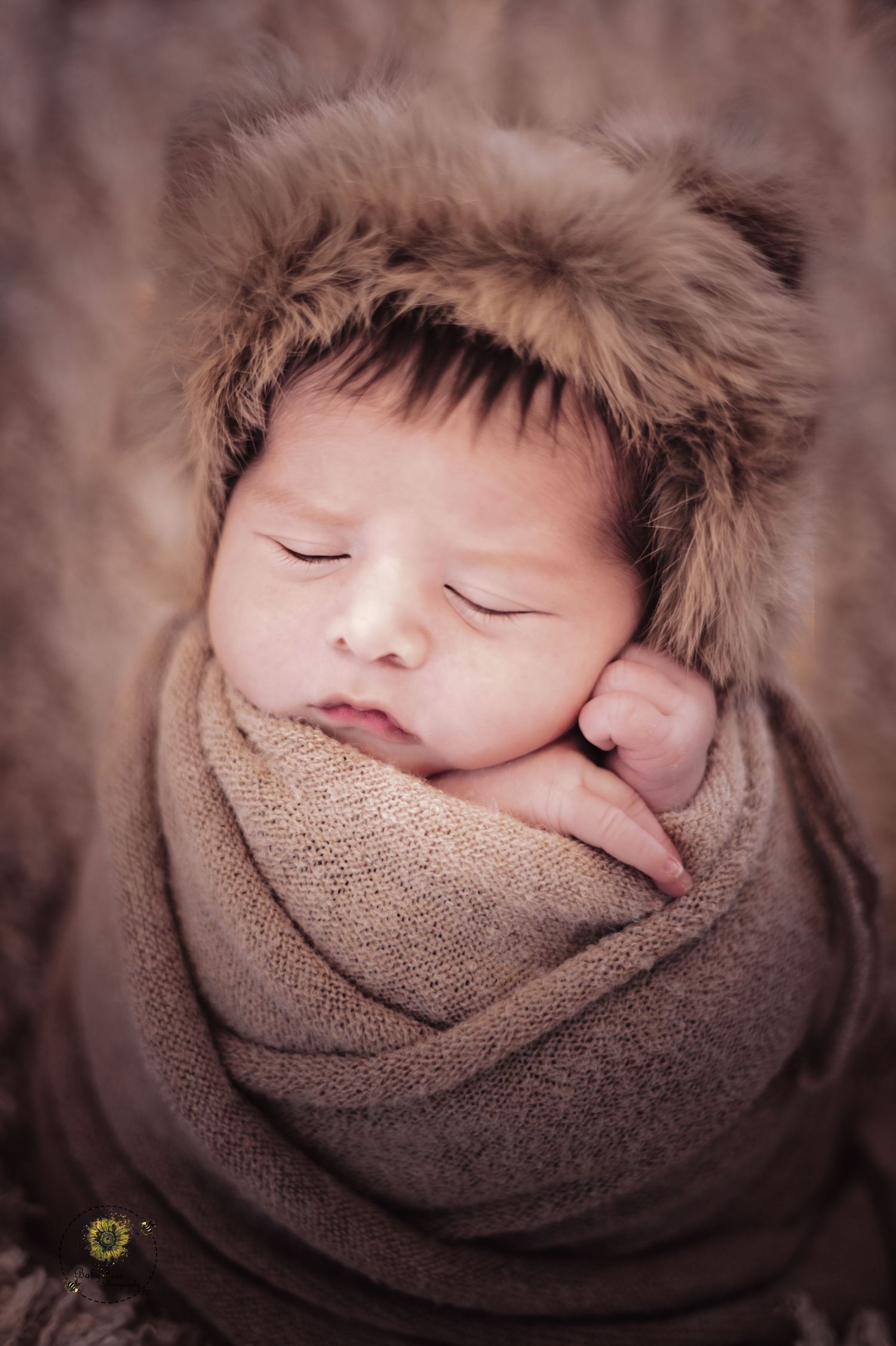 A peaceful sleeping baby bundled in a brown wrap with a furry hat in warm sepia tones.