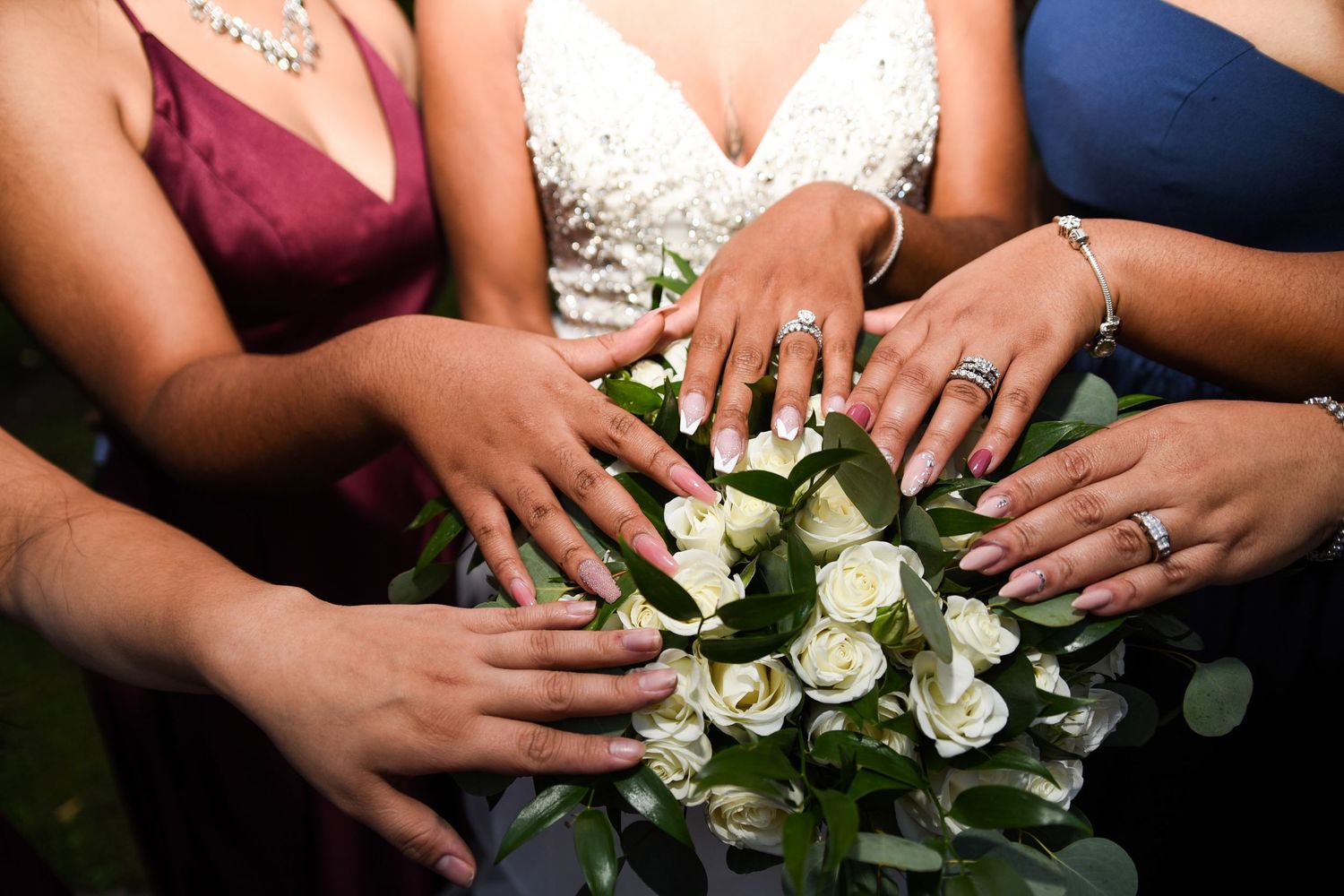 Close-up of hands displaying wedding rings alongside white rose bouquet details.