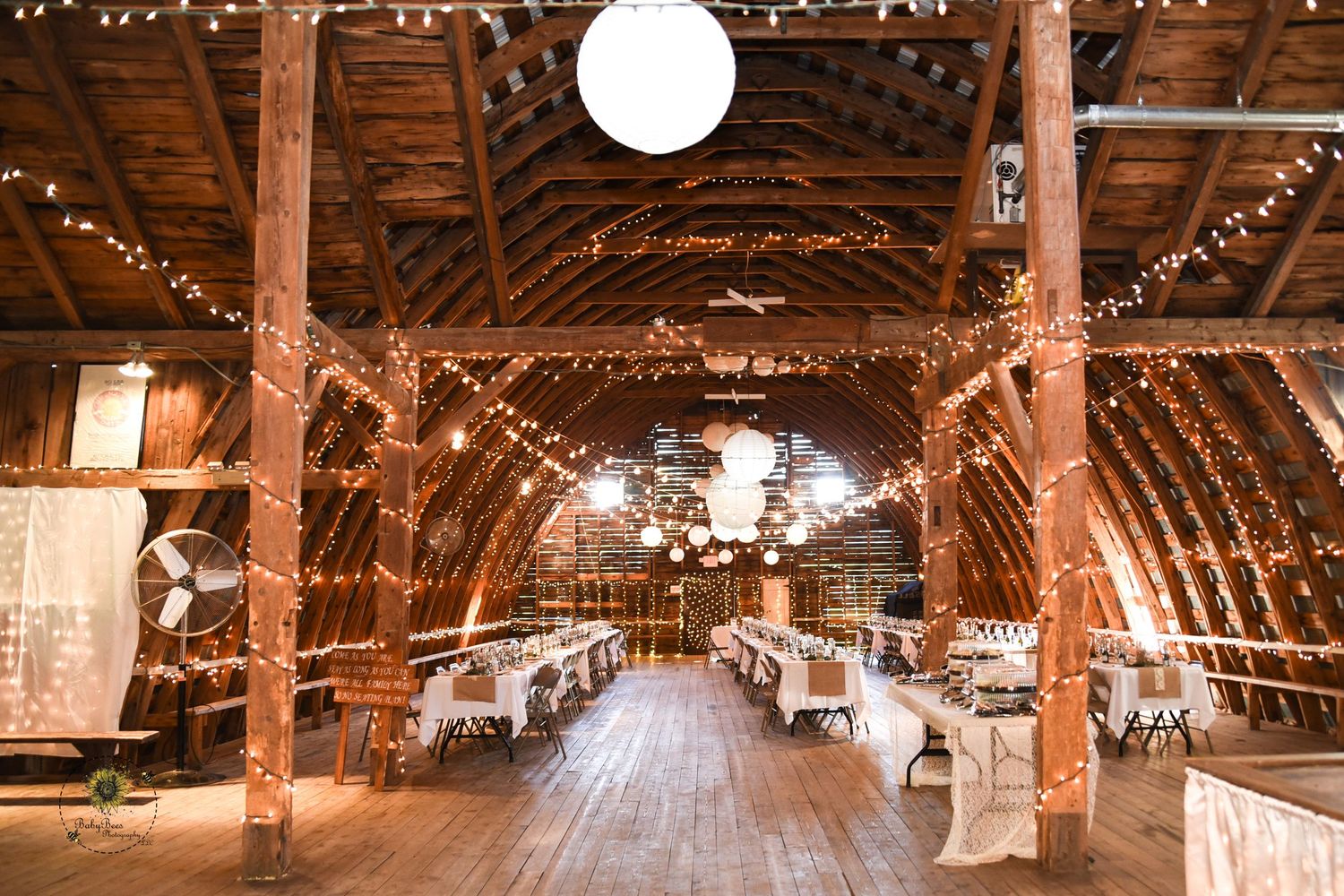 Rustic barn wedding venue interior with wooden beams and twinkling string lights creating a warm romantic atmosphere.