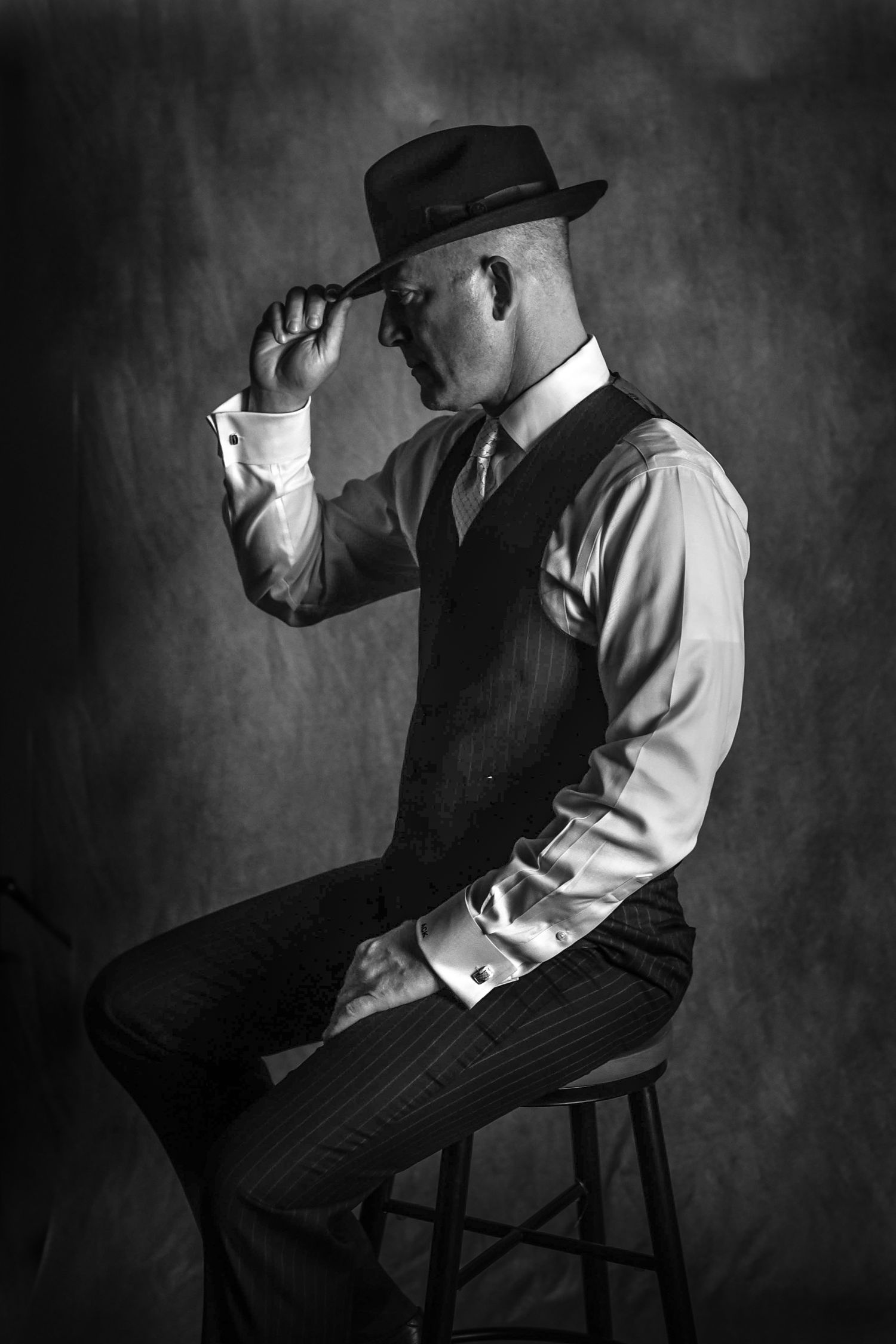 A dramatic black and white photo series showing a person in vintage attire and hat posing artistically in a chair.