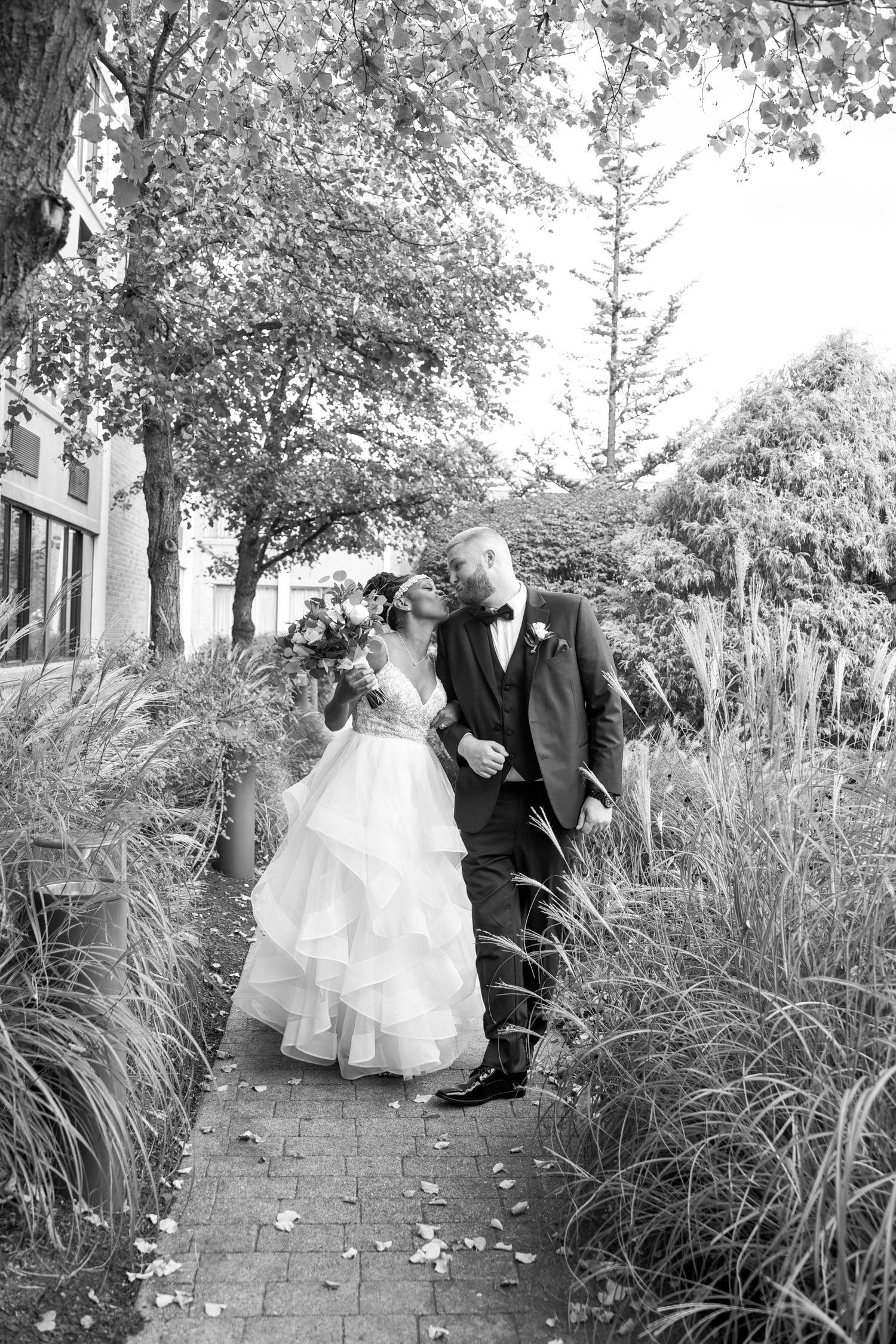A romantic wedding couple shares tender moments along a garden pathway lined with ornamental grasses.