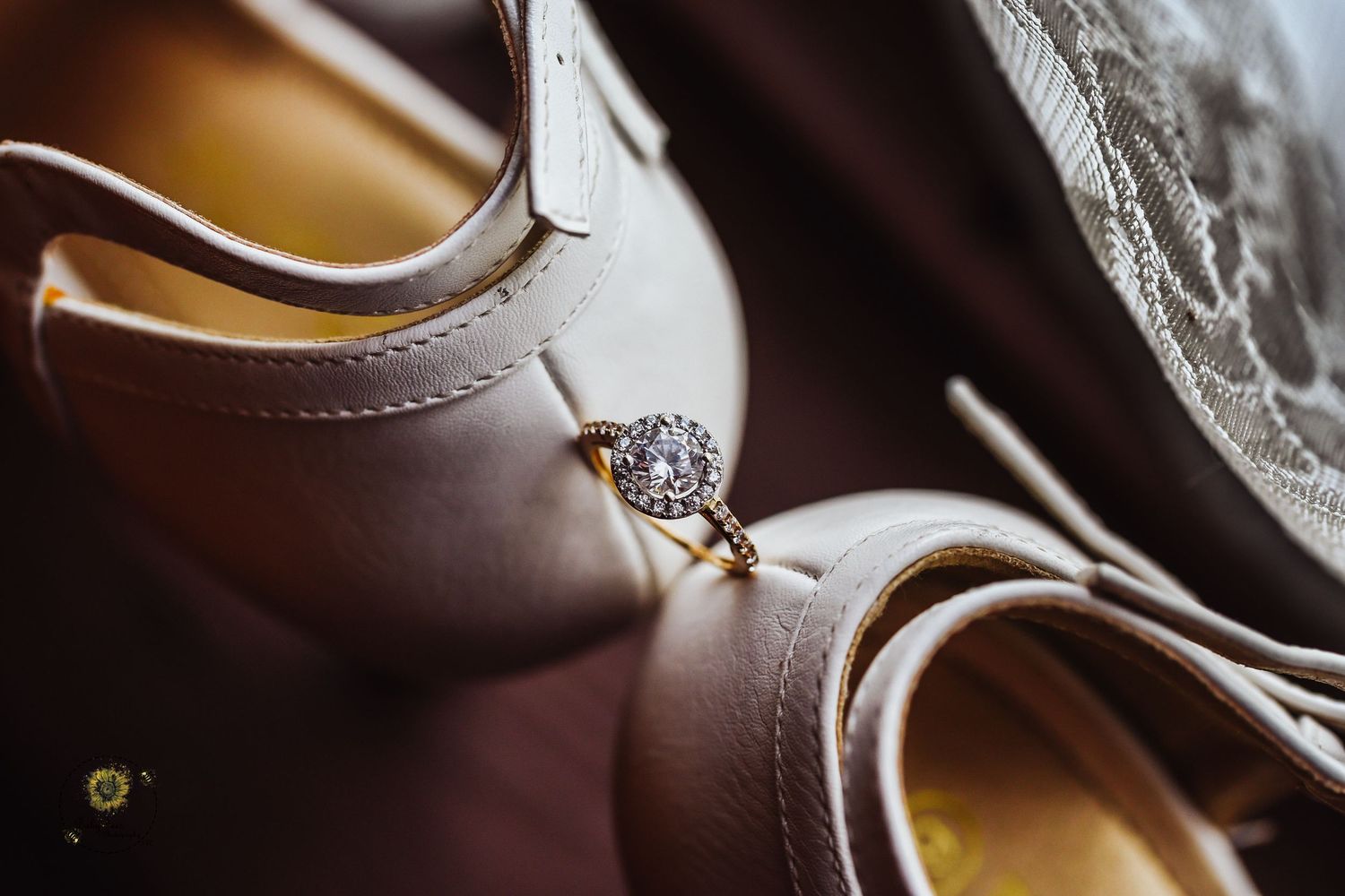 Close-up detail shot of a sparkling diamond engagement ring resting on beige wedding shoes.