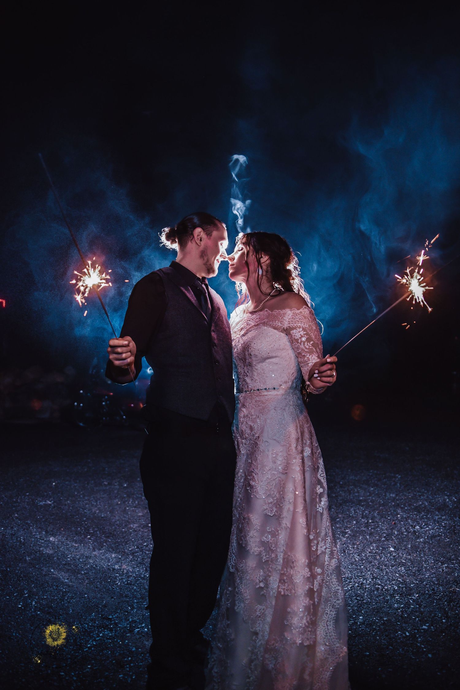 A couple holds sparklers during their nighttime wedding celebration with blue smoke effects.