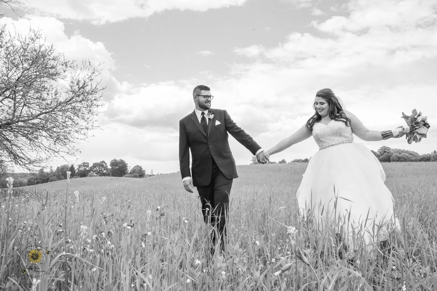 Black and white photo of newlyweds running joyfully through a field.
