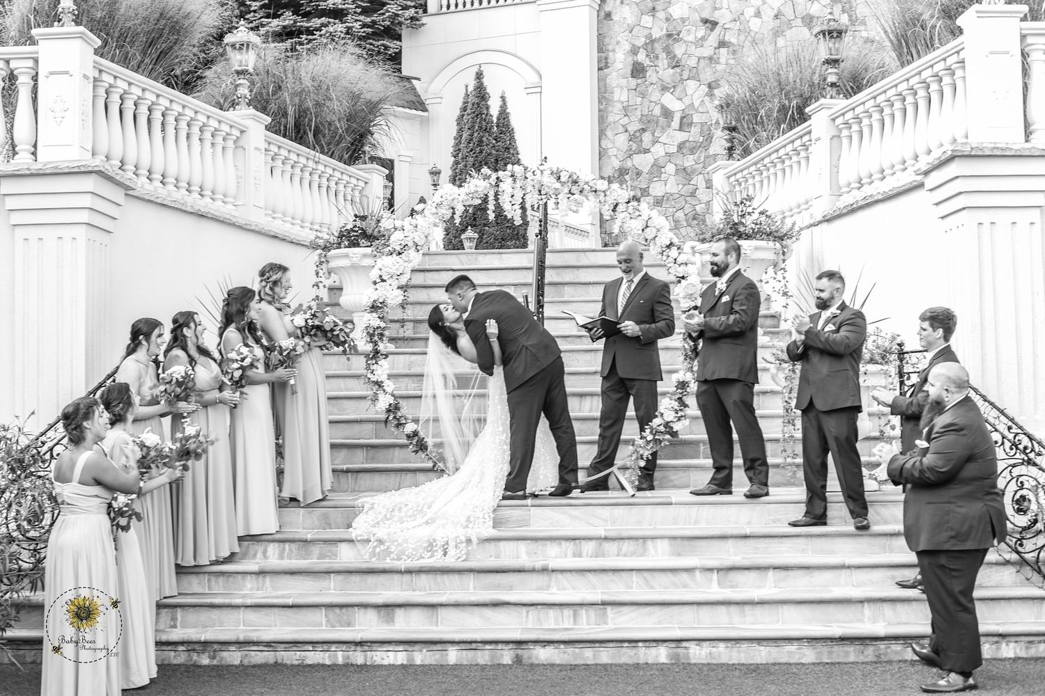 Wedding guests gather on elegant white stone staircase for group photos.