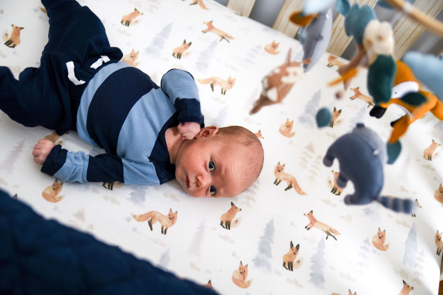 Baby lying on white blanket surrounded by scattered orange and brown autumn leaf cutouts for seasonal photo shoot.
