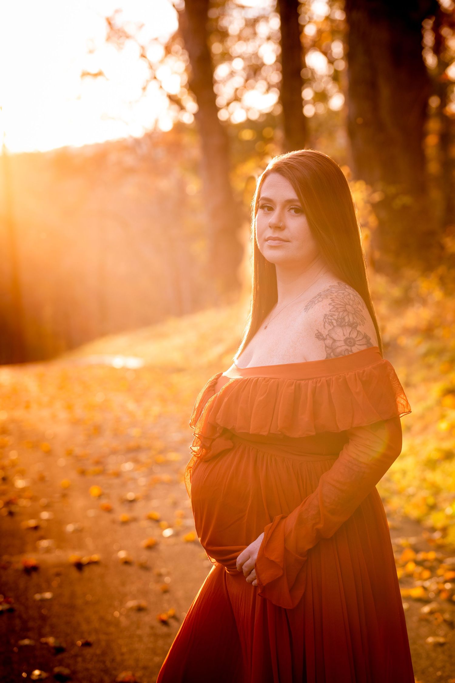 A person in a dark dress poses in a golden autumn forest during sunset, creating a dreamy atmospheric portrait.