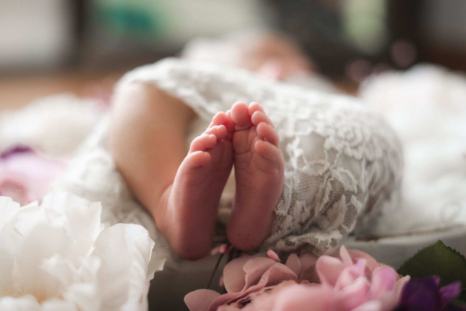 Close up of tiny newborn baby feet wrapped in soft white blankets and pink floral decorations.
