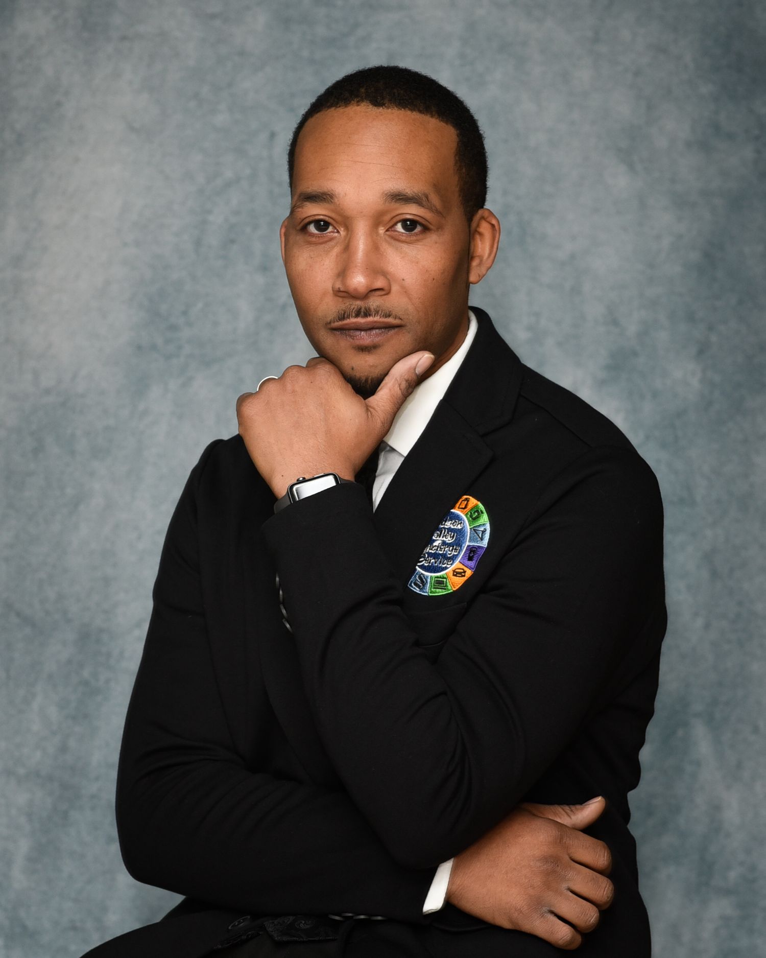 Professional portrait series against gray backdrop showing person in dark suit and Olympic pin.