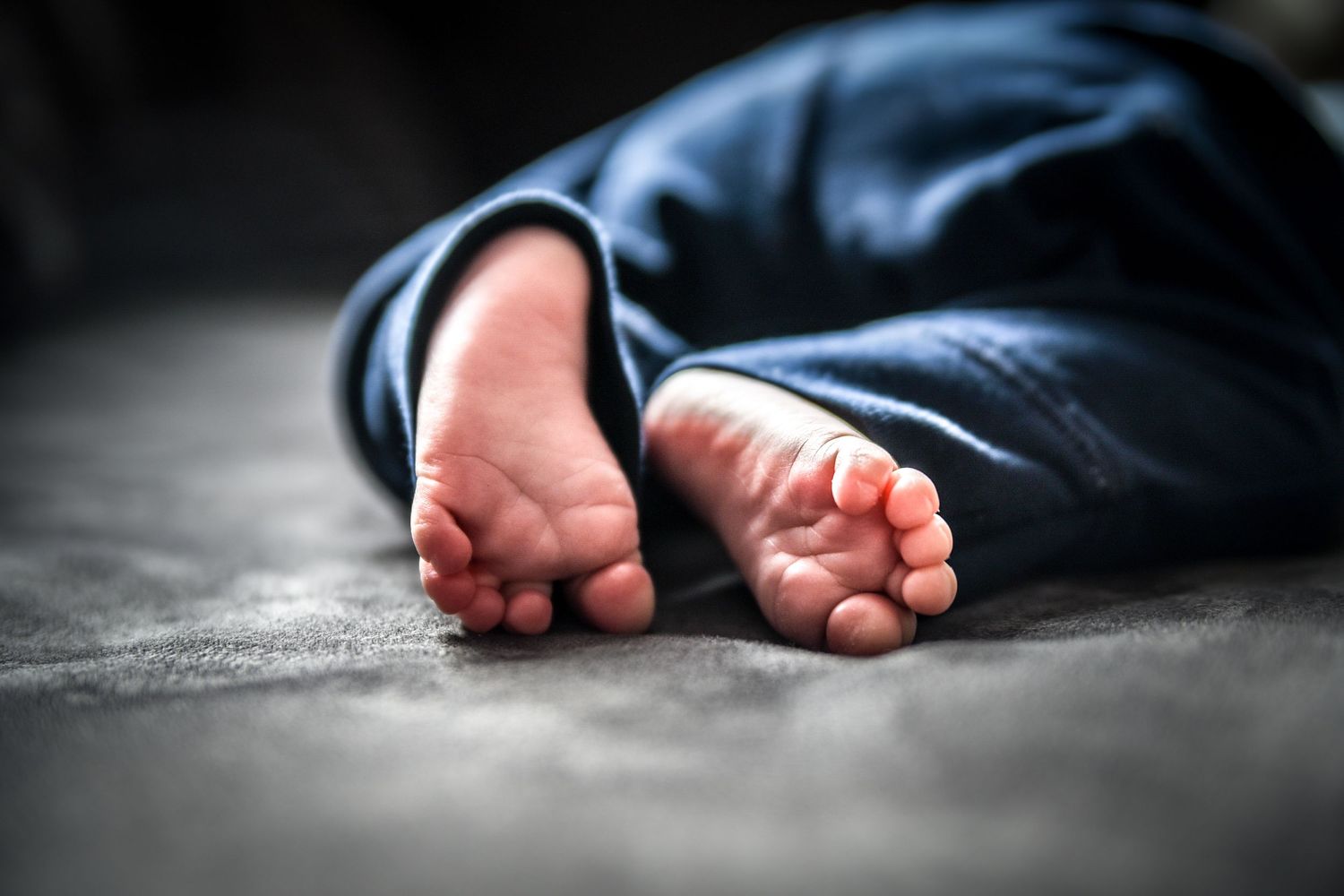 A person's feet in dark clothing lying motionless on a concrete floor in dramatic lighting.
