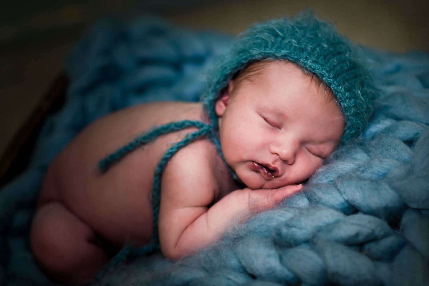 A sleeping newborn baby wrapped in soft blue blankets lies peacefully in a dimly lit room.