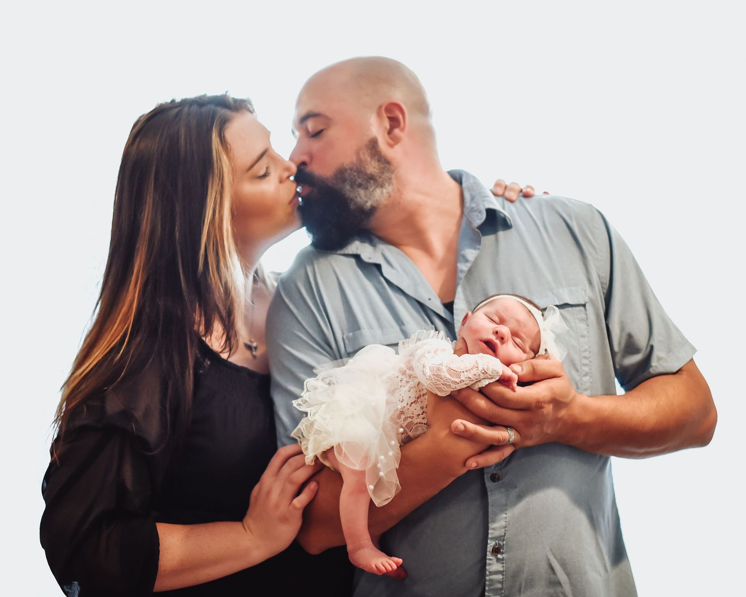 A couple shares an intimate moment while holding their newborn baby wearing a white tutu dress.
