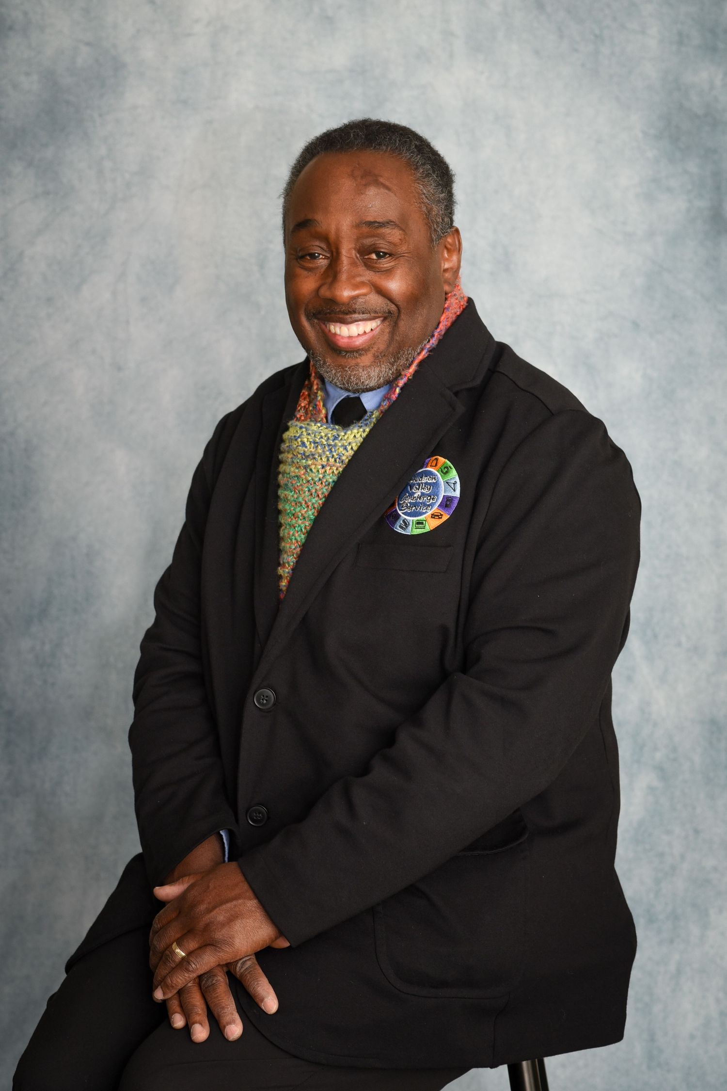 Professional studio portraits showing a person in a black suit jacket with a patterned tie against a gray background.