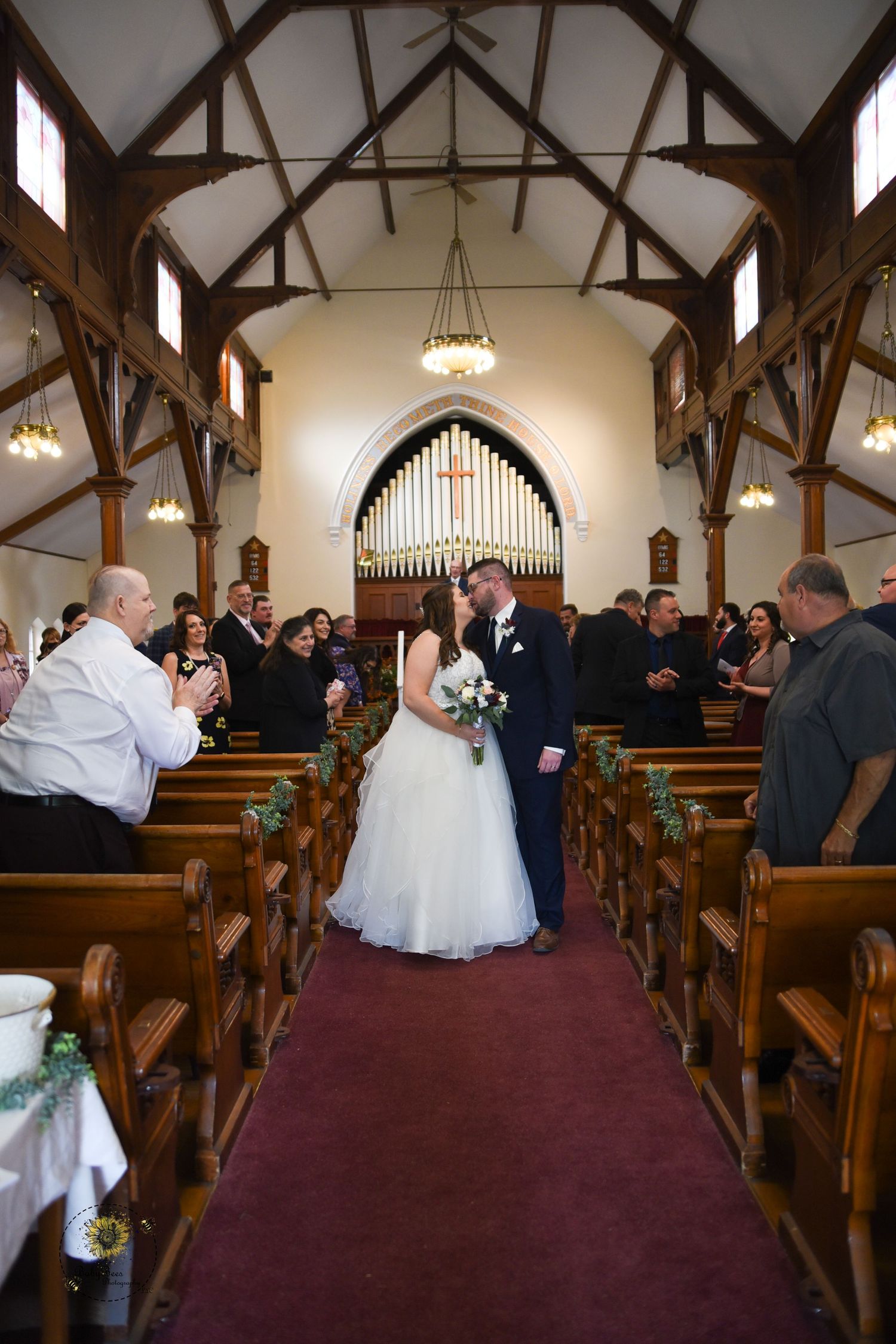Wedding ceremony in a historic chapel with wooden beams and stained glass windows.