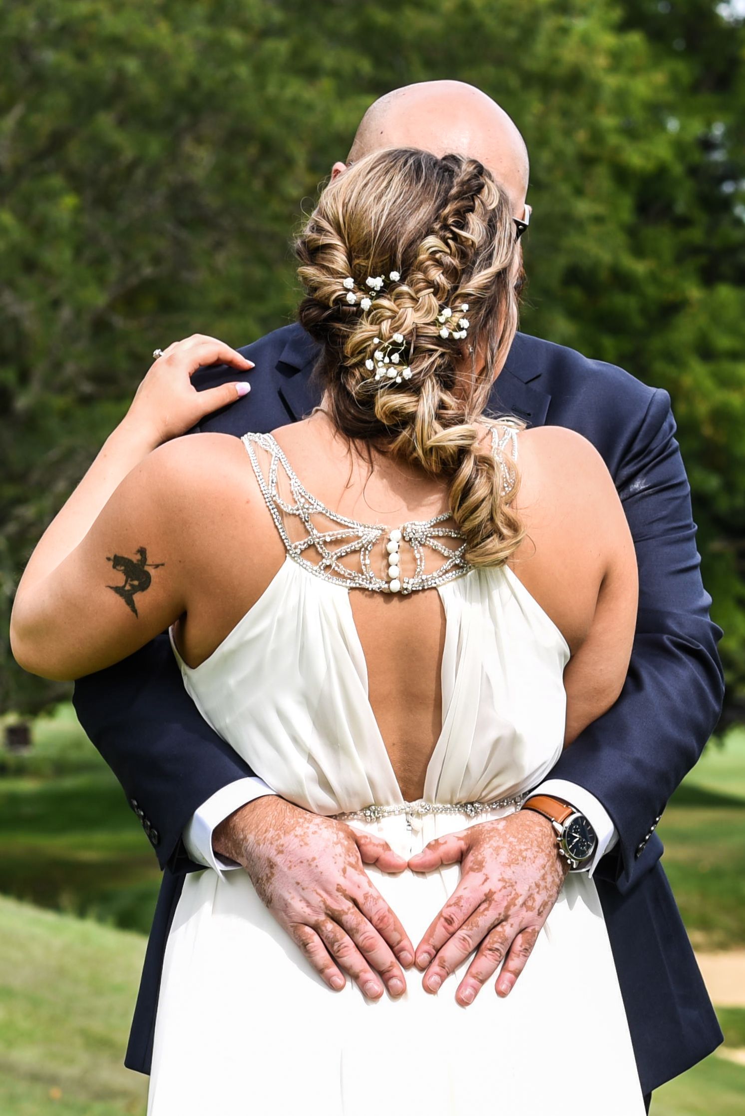 Back view of wedding couple embracing outdoors with ornate hair accessories visible.