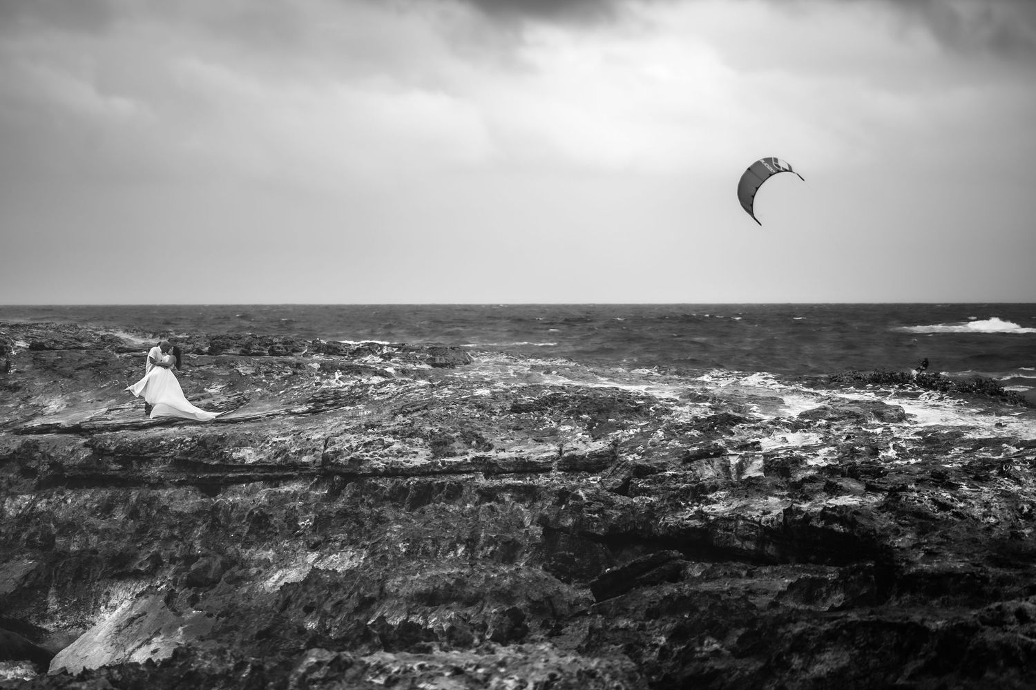 Moody black and white seascape showing rugged coastal rocks and crashing waves.