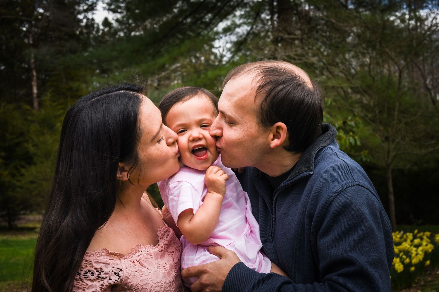 A couple shares tender moments with their baby girl in a park setting during a springtime photo session.