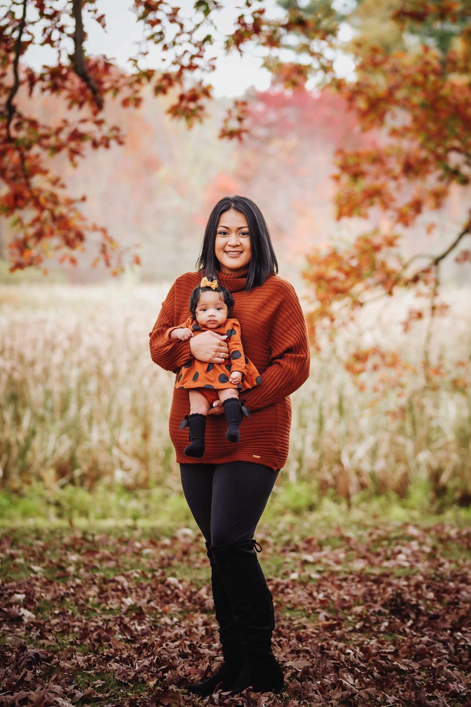 A photographer in a rust-colored sweater takes photos outdoors among autumn foliage and fallen leaves.