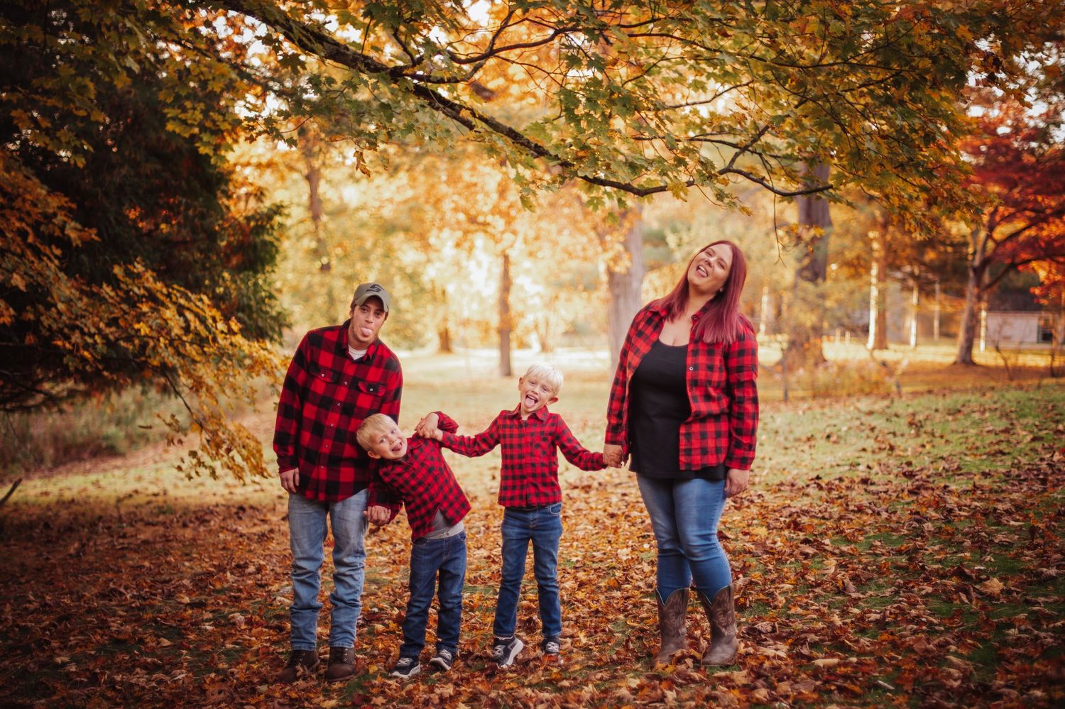 A family wearing red plaid shirts walks together through a golden autumn forest during sunset.