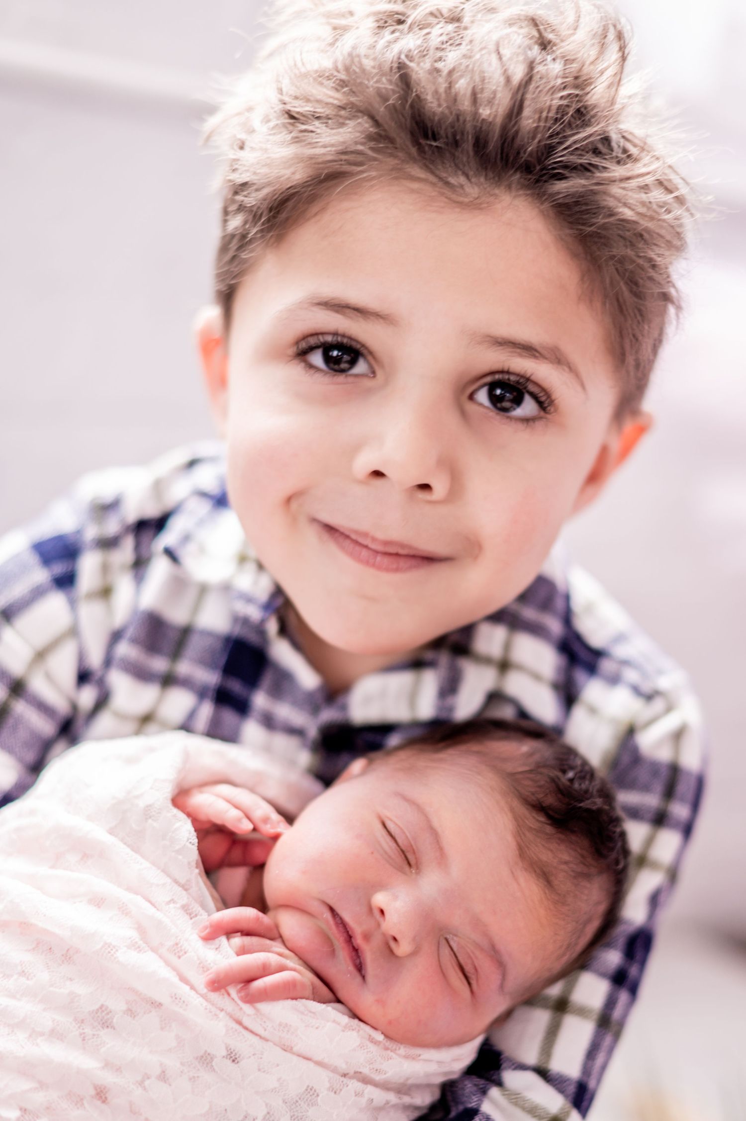 A series of intimate newborn baby photos showing tender moments with an older sibling in a plaid shirt.