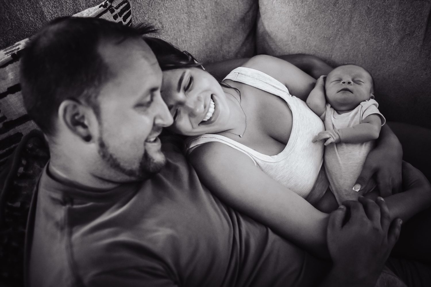 A family rests together on a couch in an intimate black and white portrait.
