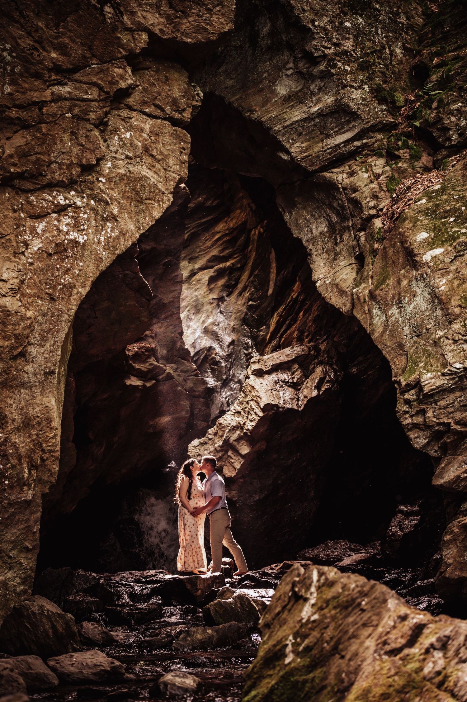 Two people stand embracing in silhouette against dramatic lighting inside a rocky cave entrance.