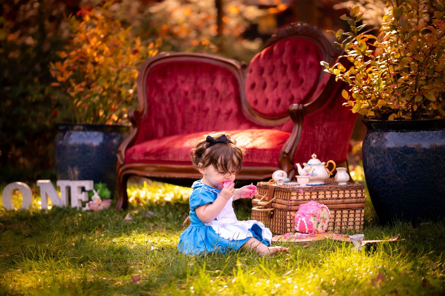 Decorative outdoor photo setup with vintage red velvet couch and props in golden autumn sunlight.