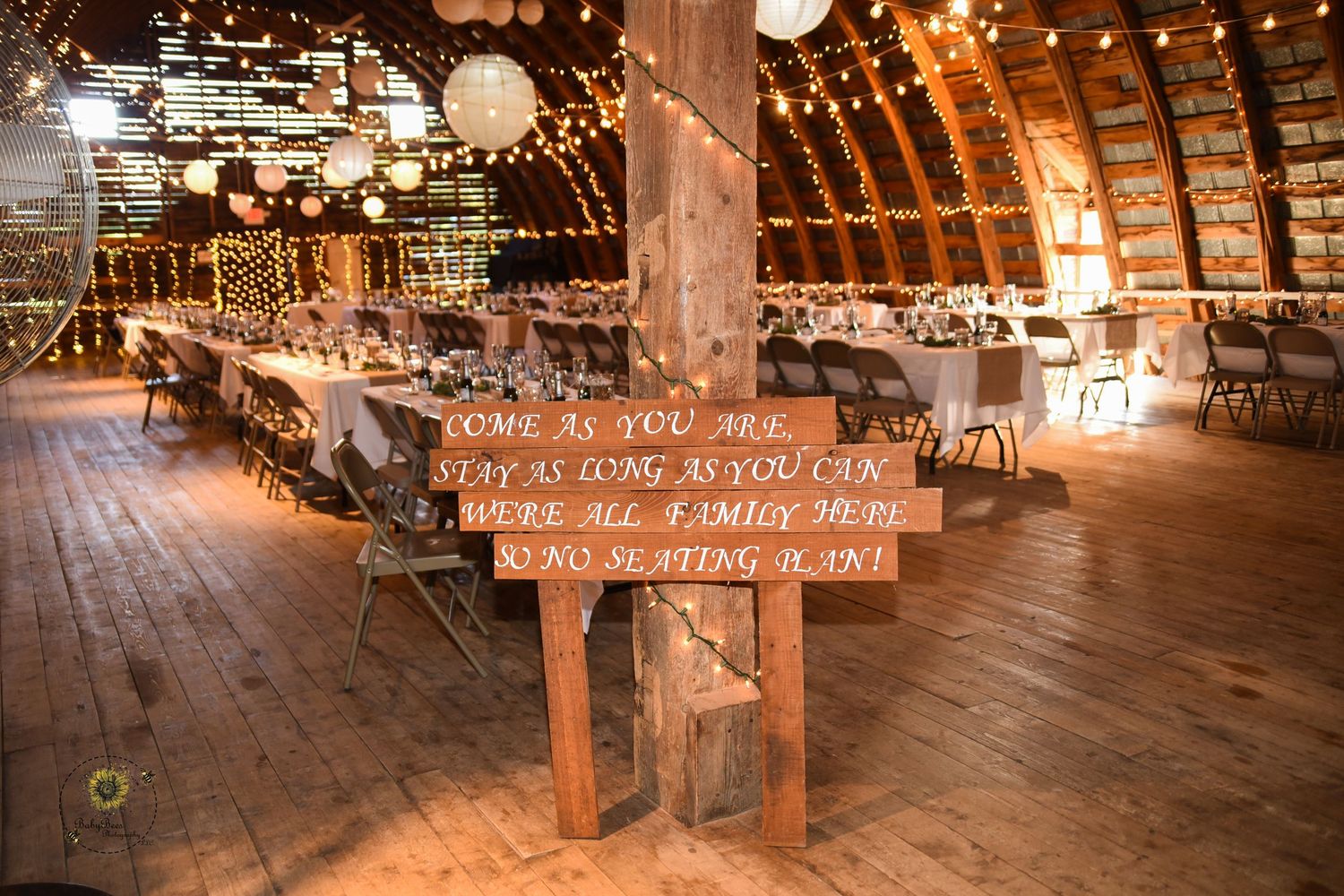 Wooden wedding sign with romantic text displayed in a rustic barn venue with string lights.