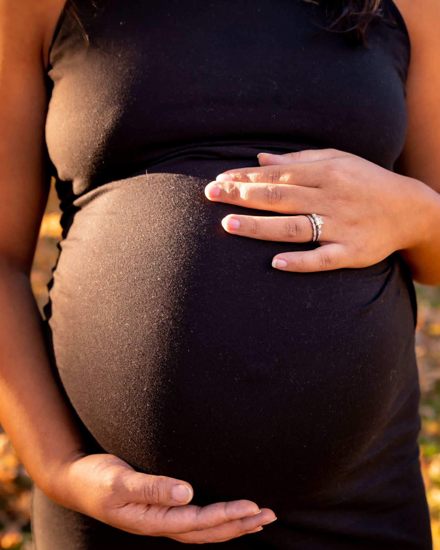 Hands gently cradling a pregnant belly in a maternity photoshoot against a warm sunset background.