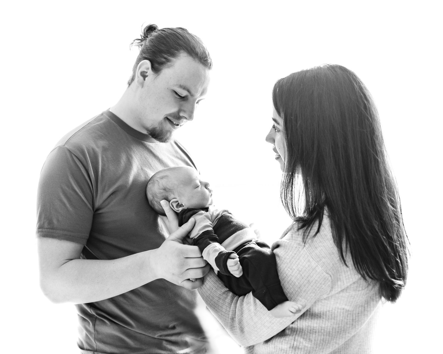 A black and white portrait of parents lovingly holding their newborn baby in a tender family moment.