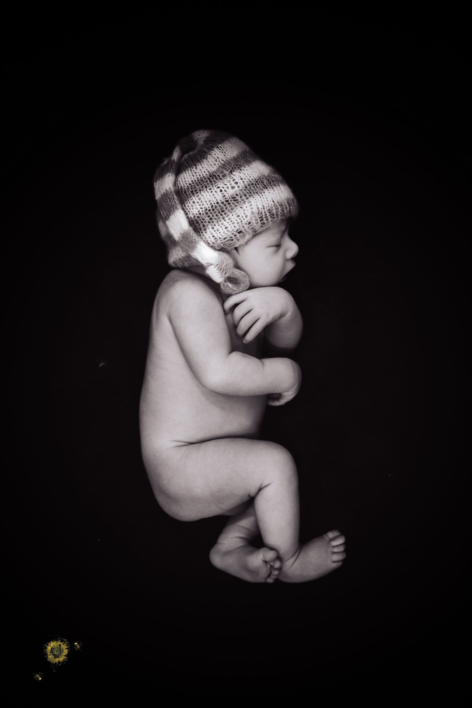 A dramatic black and white portrait of a sleeping newborn wearing a knit cap against dark background.