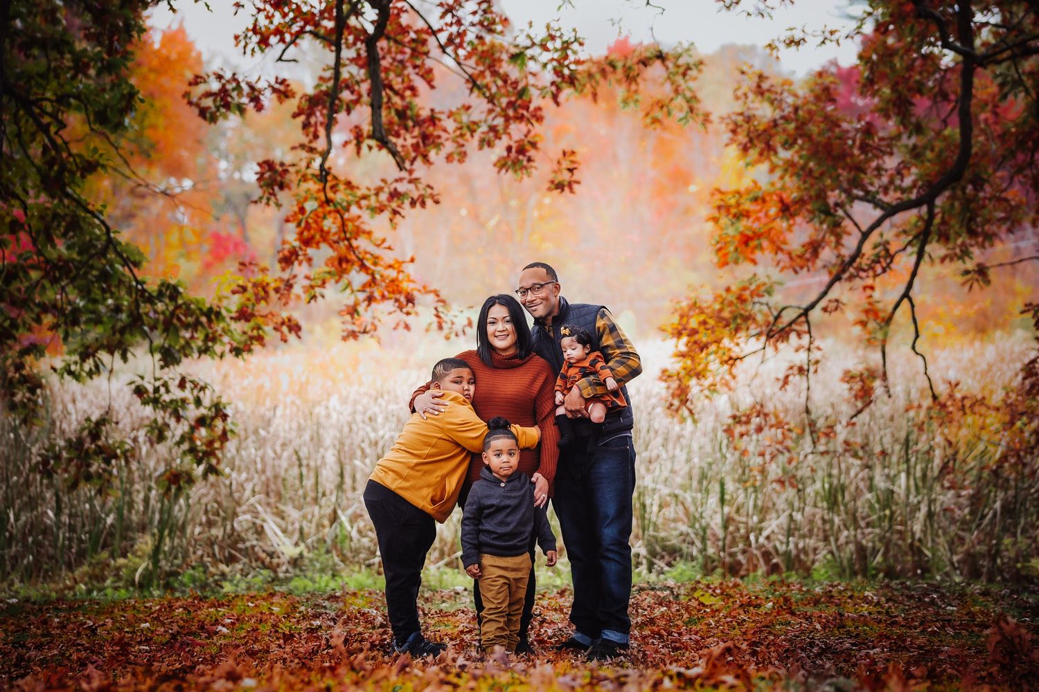 A family embraces outdoors during autumn with colorful fall foliage and golden light in the background.