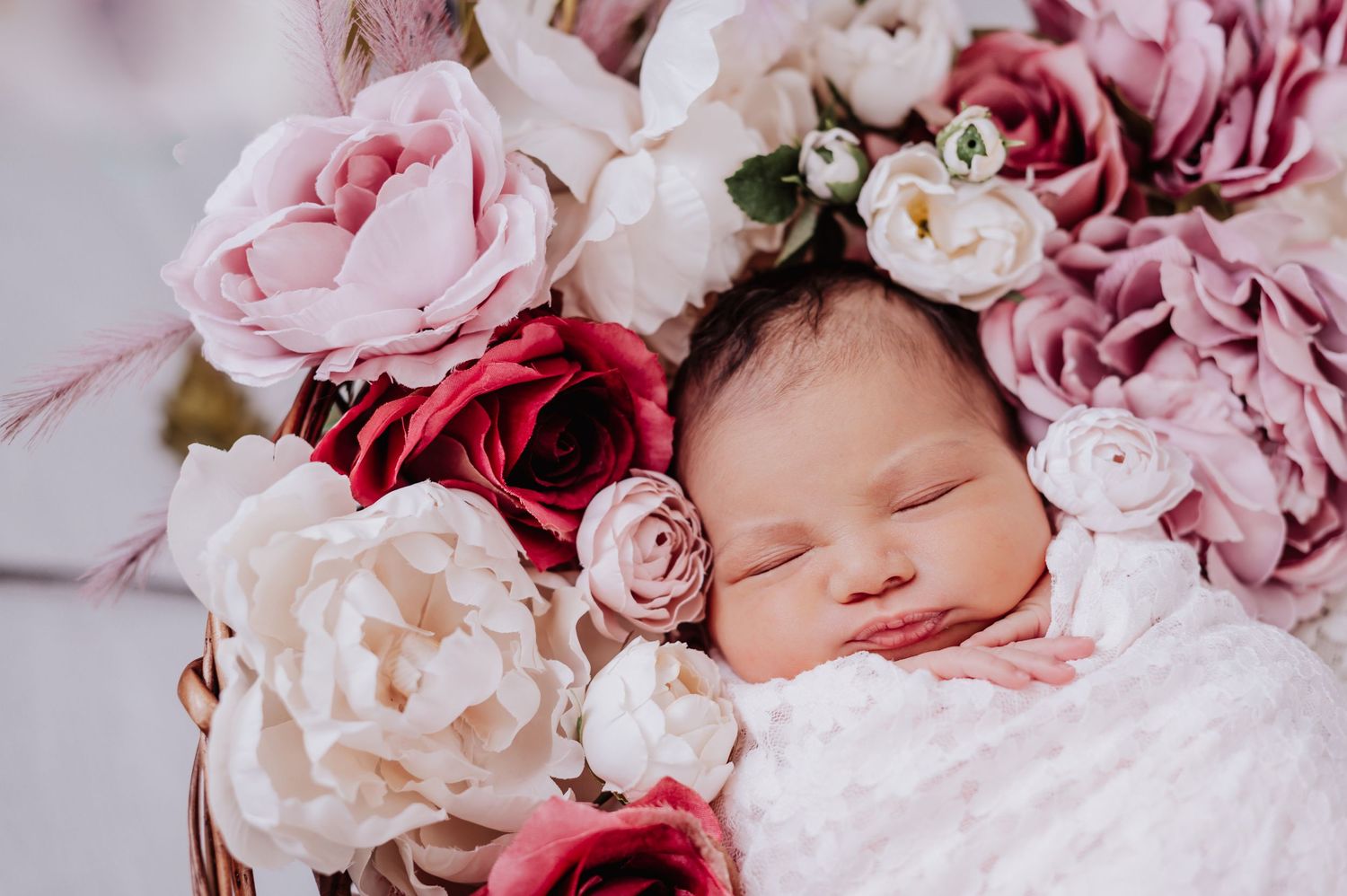 Sleeping newborn nestled among pink and white roses and peonies in dreamy floral setting.